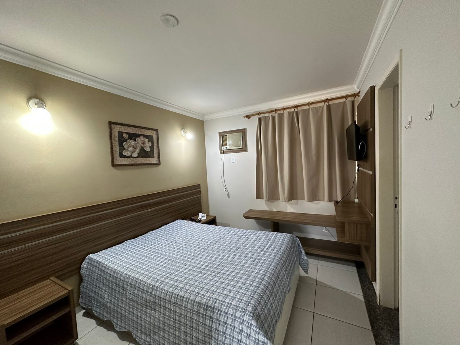 Een hotelkamer met een bed, nachtkastje, tv aan de muur en een raam met gordijnen.