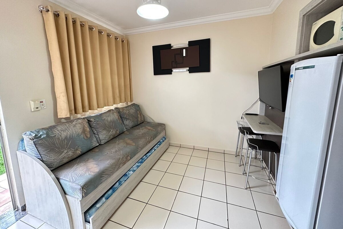 Ein kompakter Wohnraum mit einer Couch, einem kleinen Tisch, einem Kühlschrank und einem Deckenventilator.