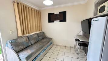 A compact living space with a sofa, a small table, a refrigerator, and a ceiling fan.