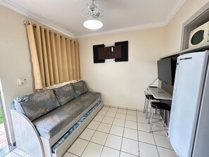 A compact living space with a sofa, a small table, a refrigerator, and a ceiling fan. - DiRoma International Resort Via Caldas (Caldas Novas)