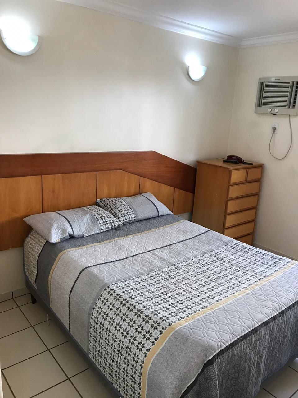 Een slaapkamer met een bed, een houten hoofdbord, een dressoir en een wandairconditioner.