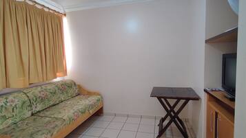 A room with a sofa, a small table, a television, and a cabinet.