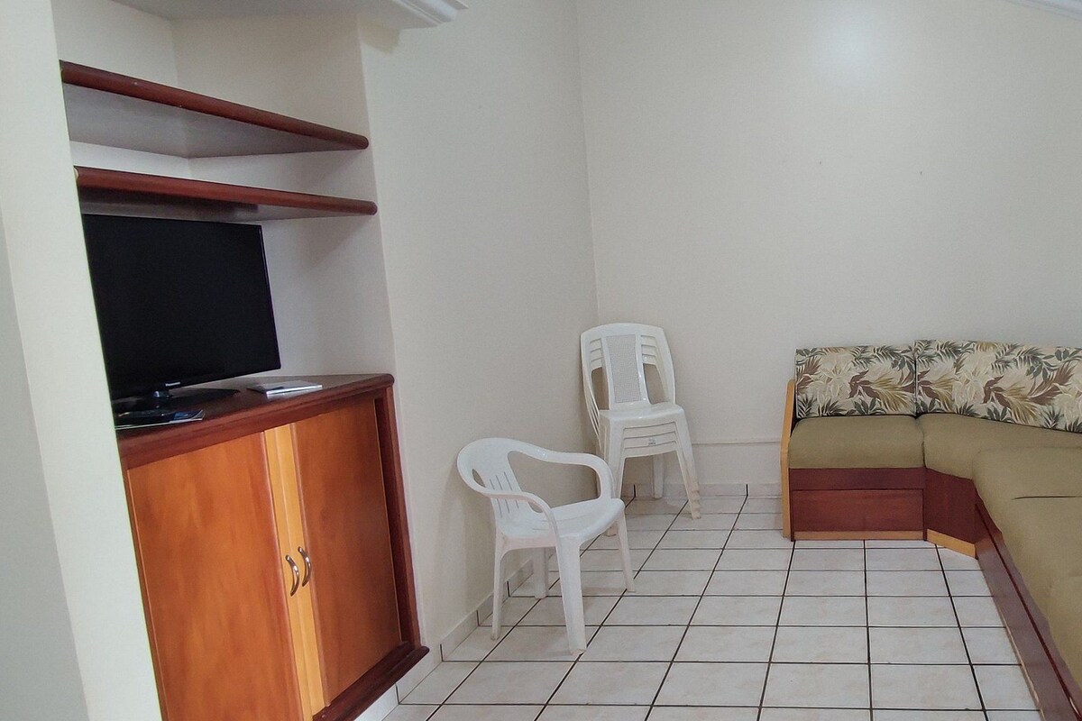 Ein Wohnzimmer mit Sofa, Fernseher, Schrank und einem Fenster mit Vorhängen.