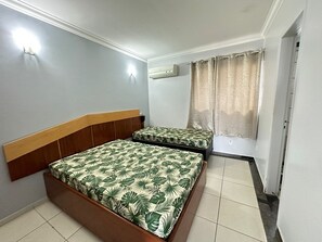 Une chambre avec deux lits, une fenêtre avec des rideaux, un appareil de climatisation et un luminaire fixé au mur.
