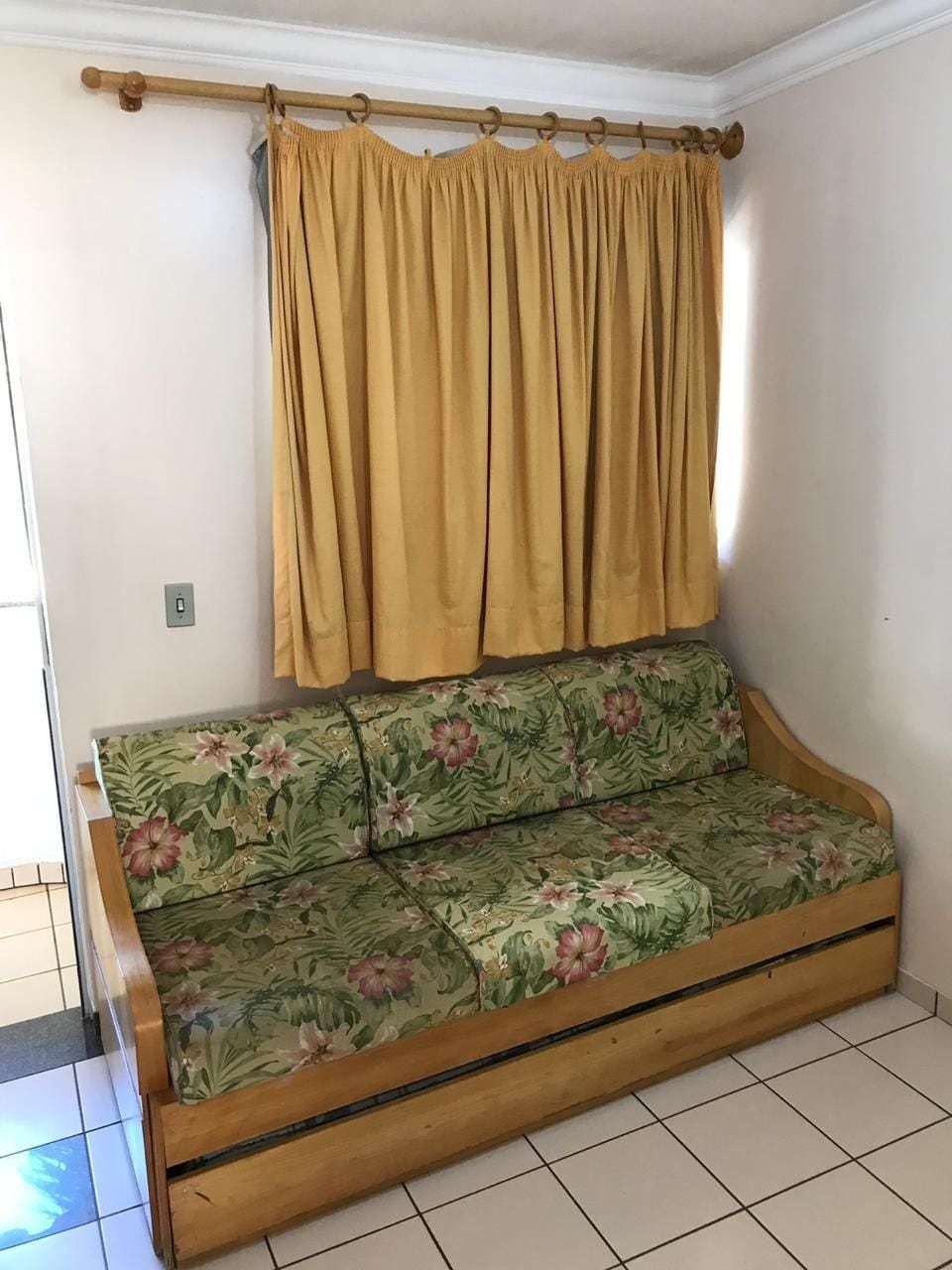 A sofa with floral upholstery, a wooden frame, and a curtain rod above it.