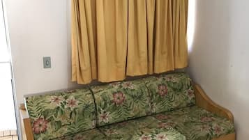 A sofa with floral upholstery, a wooden frame, and a curtain rod above it.