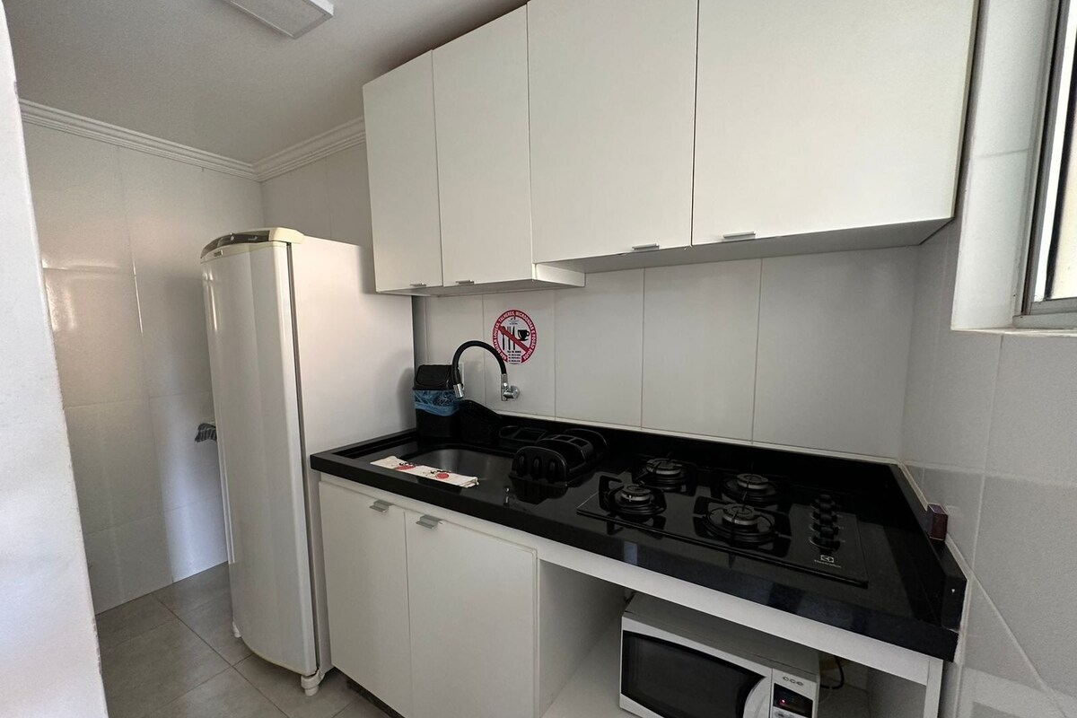 Eine kleine Küche mit weißen Schränken, einer schwarzen Arbeitsplatte, einer eingebauten Mikrowelle und einem Gasherd.