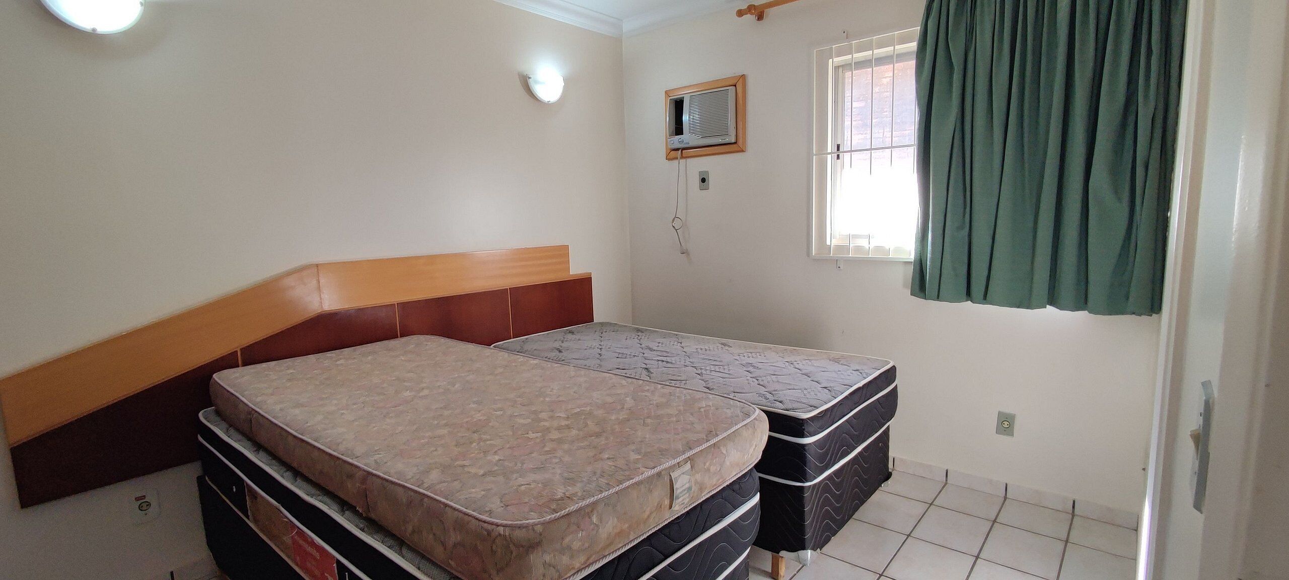 Een kamer met een bed, een raam met gordijnen, een wandairconditioner en een lamp.