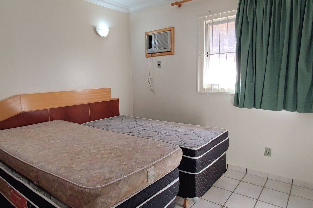 Quarto com cama, janela com cortinas, ar-condicionado na parede e luminária.