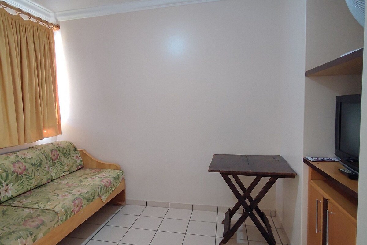 A room with a sofa, a small table, a television, and a cabinet.