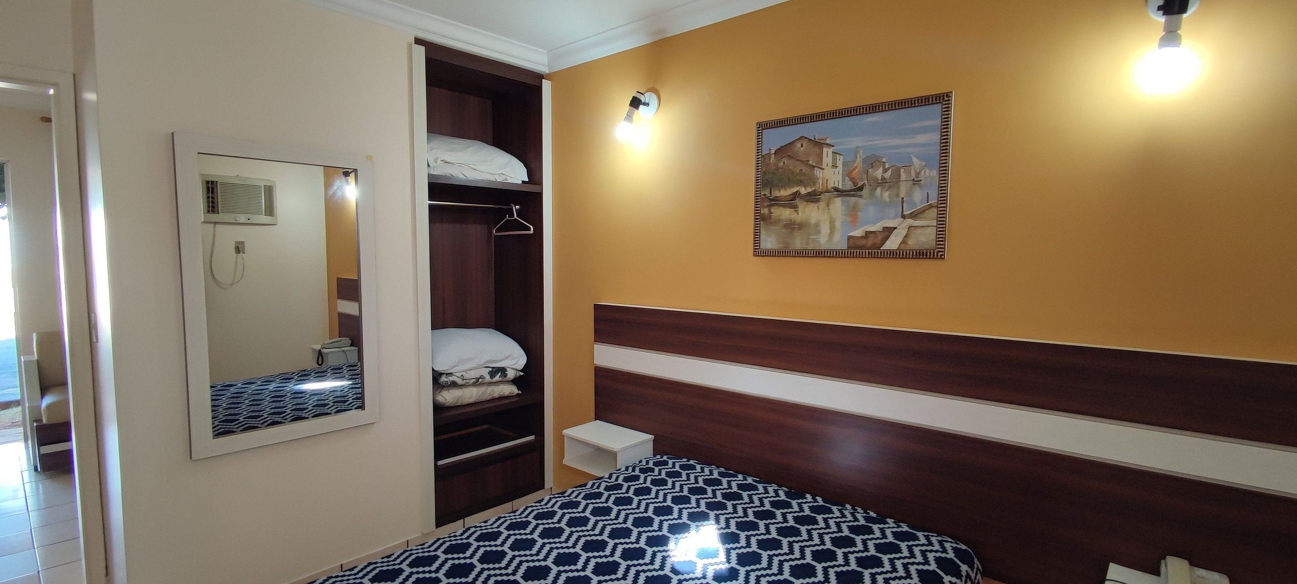 Quarto com cama, guarda-roupa, mesa de cabeceira, espelho e um quadro na parede.