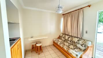 Quarto com sofá, ventilador de teto, pequena mesa com banquetas, janela com cortinas e porta que dá para o exterior.