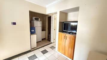 A compact kitchen with a microwave, refrigerator, and a television on a wooden cabinet.