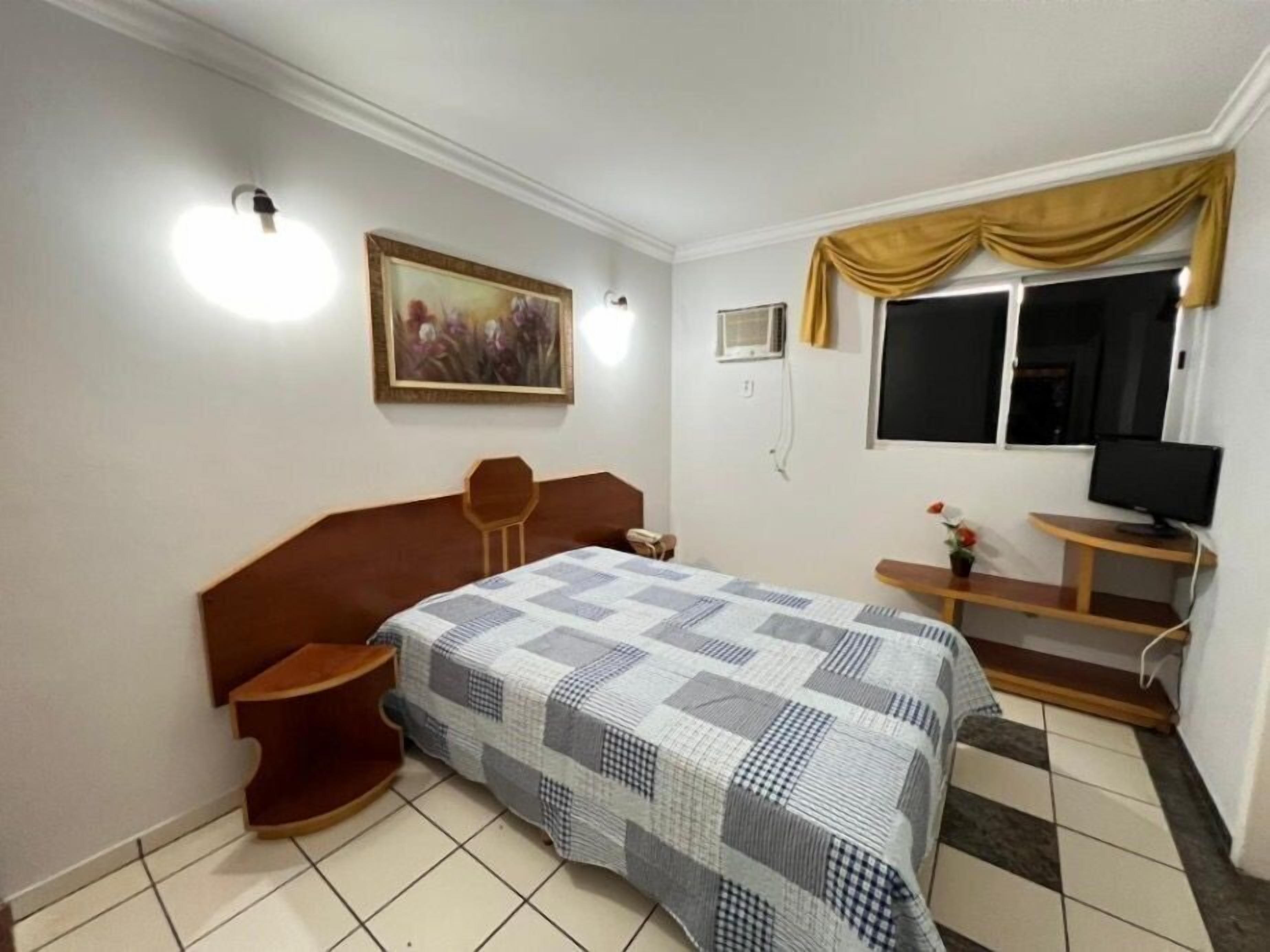 Een slaapkamer met een bed, een bureau, een stoel, een televisie en een schilderij aan de muur.