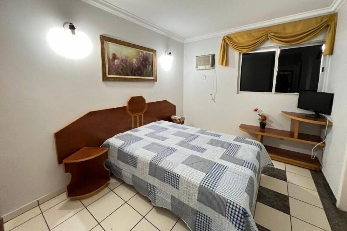 Quarto com cama, escrivaninha, cadeira, televisão e um quadro na parede.
