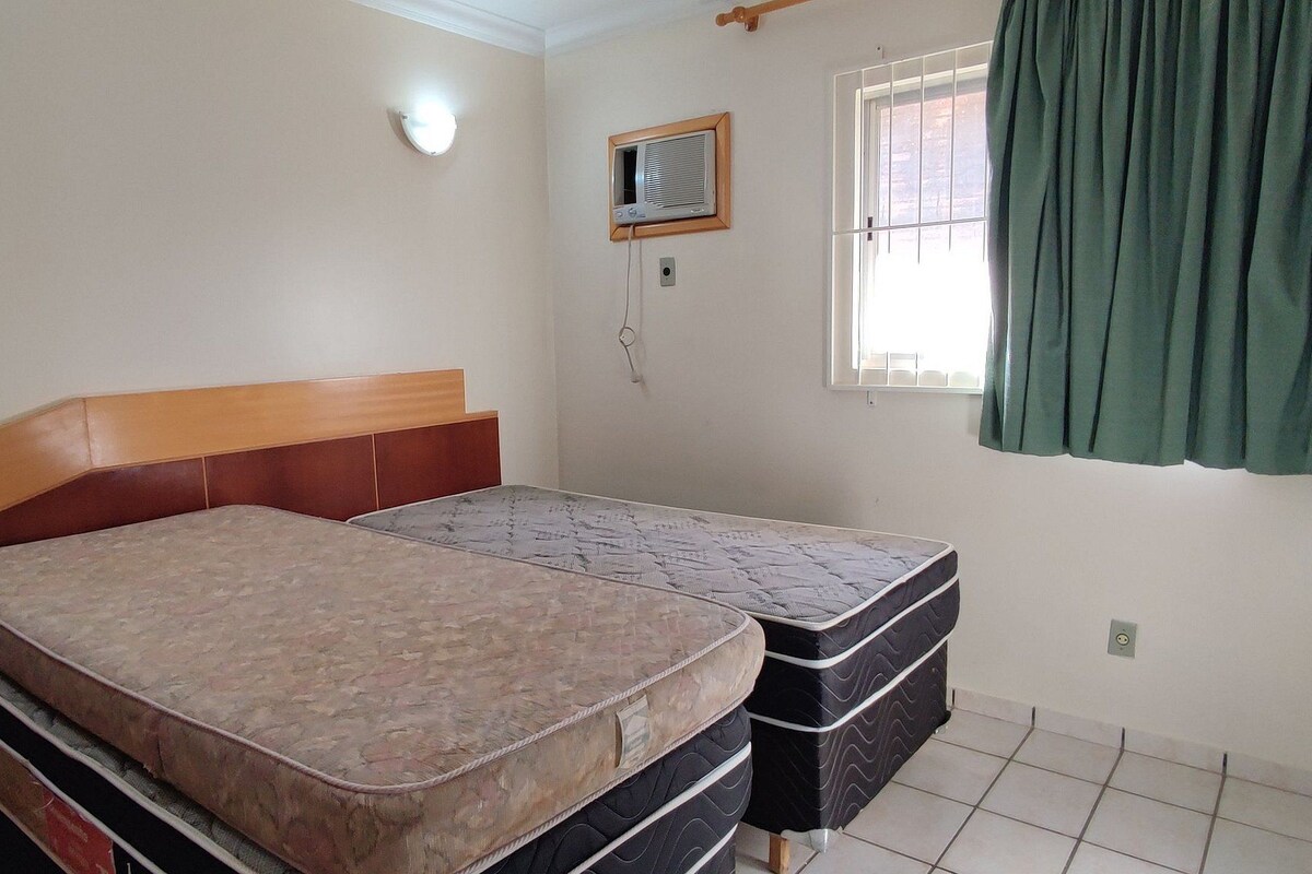 Quarto com cama, janela com cortinas, ar-condicionado na parede e luminária.
