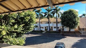 A covered parking area with a car, palm trees, and a building with a tiled roof. - DiRoma International Resort Via Caldas (Caldas Novas)