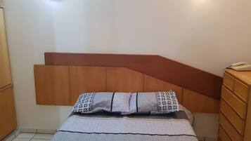 A bedroom with a bed, wooden headboard, bedside tables, and wall-mounted lights.
