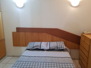 A bedroom with a bed, wooden headboard, bedside tables, and wall-mounted lights. - DiRoma International Resort Via Caldas (Caldas Novas)