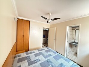 Ein Schlafzimmer mit Bett, Kleiderschrank, Deckenventilator und einem durchgehenden Türbogen einsehbaren Badezimmer.