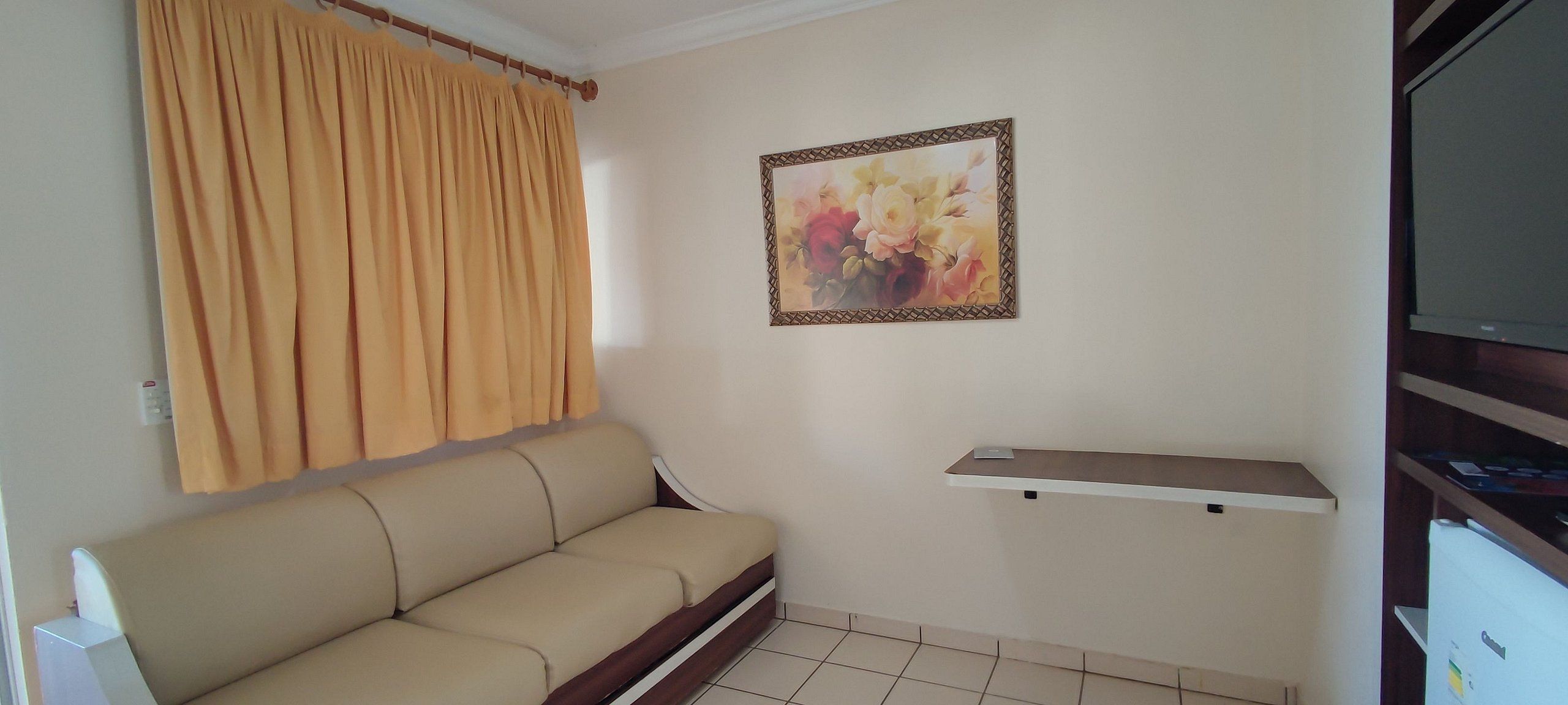 A room with a beige sofa, a wall-mounted shelf, a painting, and a television.
