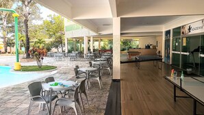 An outdoor patio area with tables and chairs, a pool, and a ping pong table. - DiRoma International Resort Via Caldas (Caldas Novas)