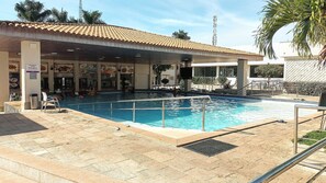 Une piscine surmontée d’un toit carrelé, une poubelle et un panneau d’affichage.