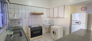 A compact kitchen with a sink, stove, microwave, and a small washing machine. - DiRoma International Resort Via Caldas (Caldas Novas)