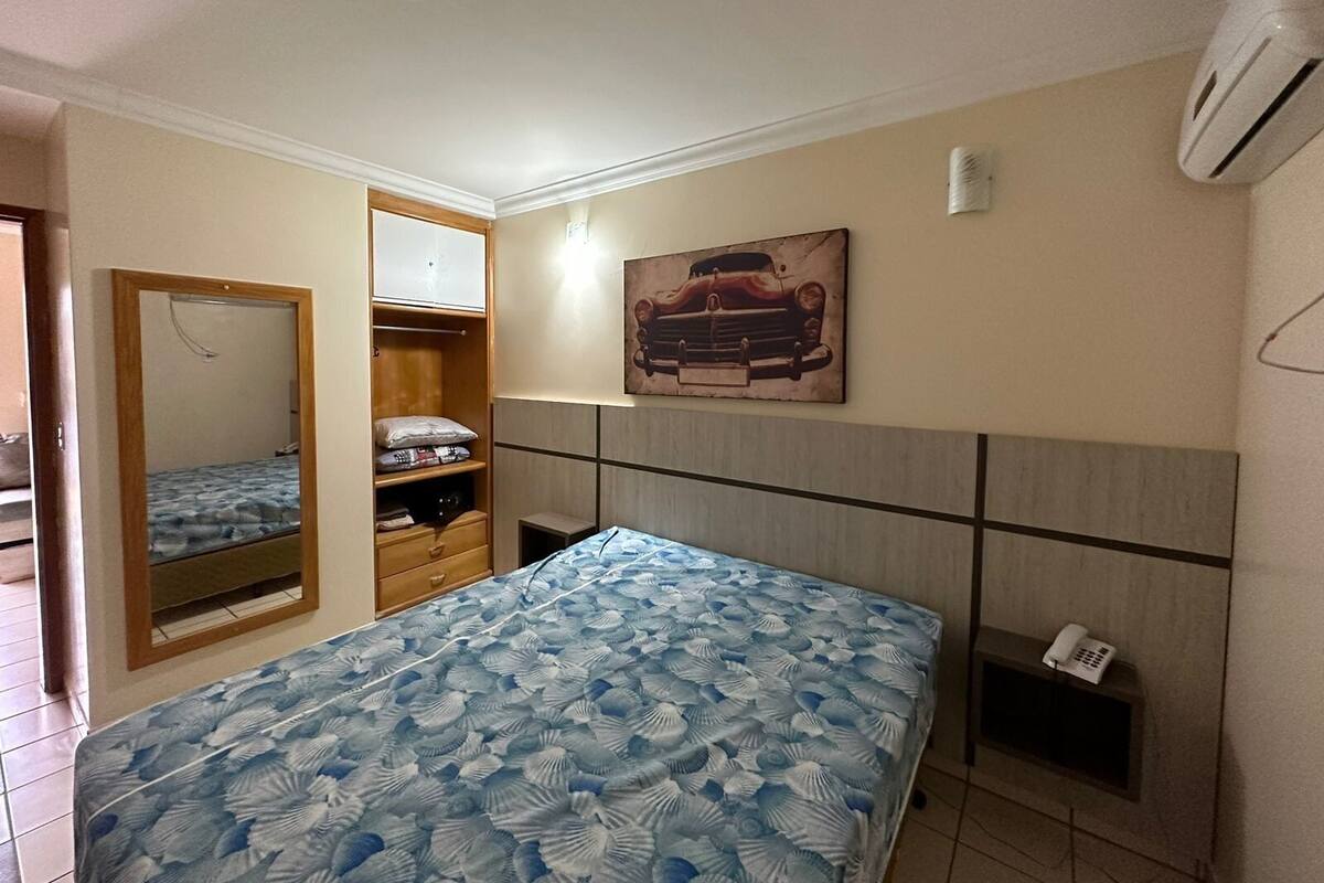 Quarto com cama, guarda-roupa, espelho, quadro e telefone em uma prateleira.