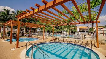Ett poolområde med träpergola, solstolar och en kristallklar, blå pool.