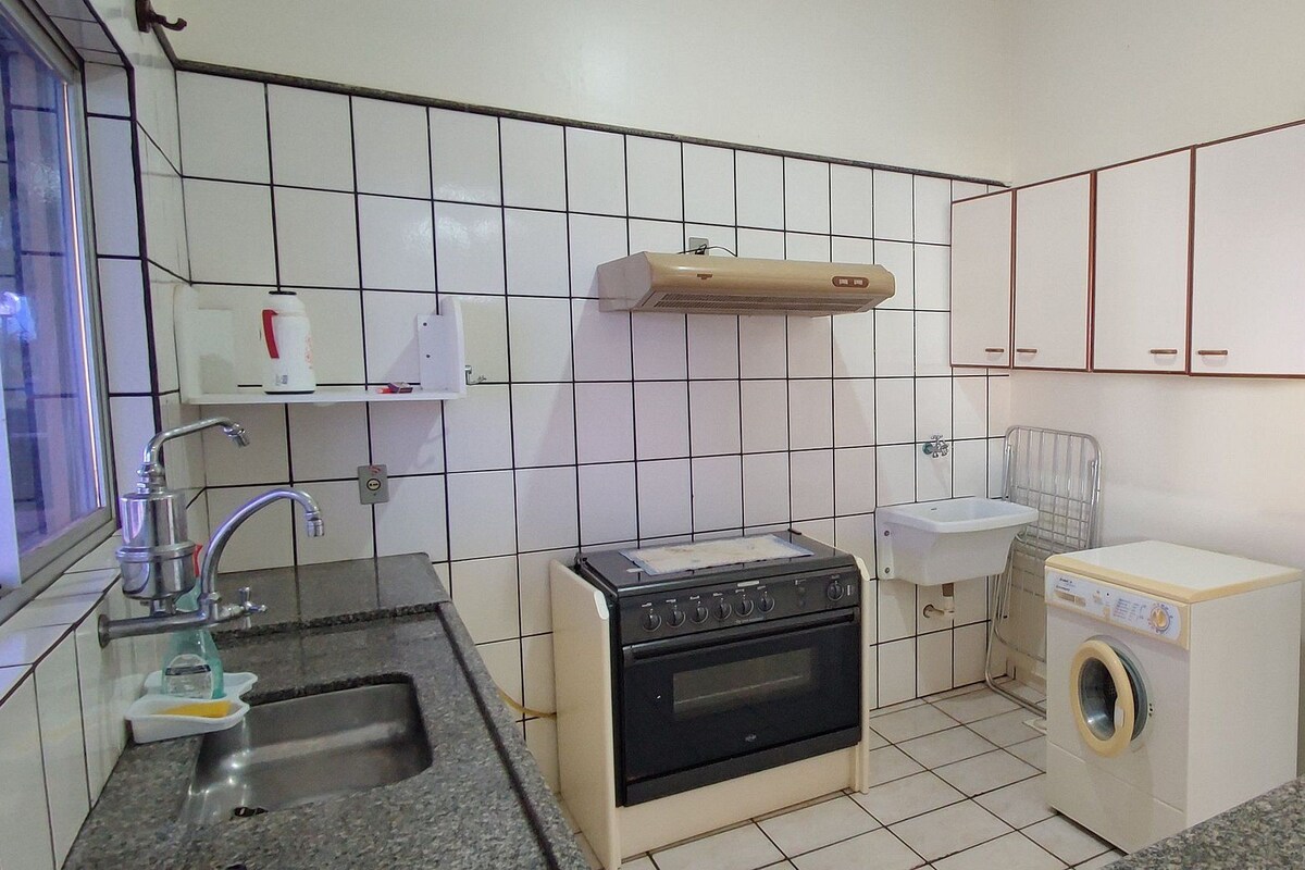 A compact kitchen with a sink, stove, microwave, and a small washing machine.