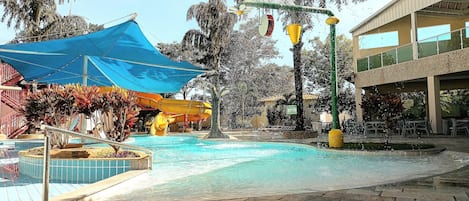 A pool area with a water slide, a blue canopy, and a building with a balcony.