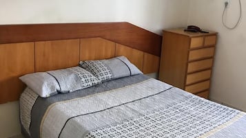 A bedroom with a bed, a wooden headboard, a dresser, and a wall-mounted air conditioner.