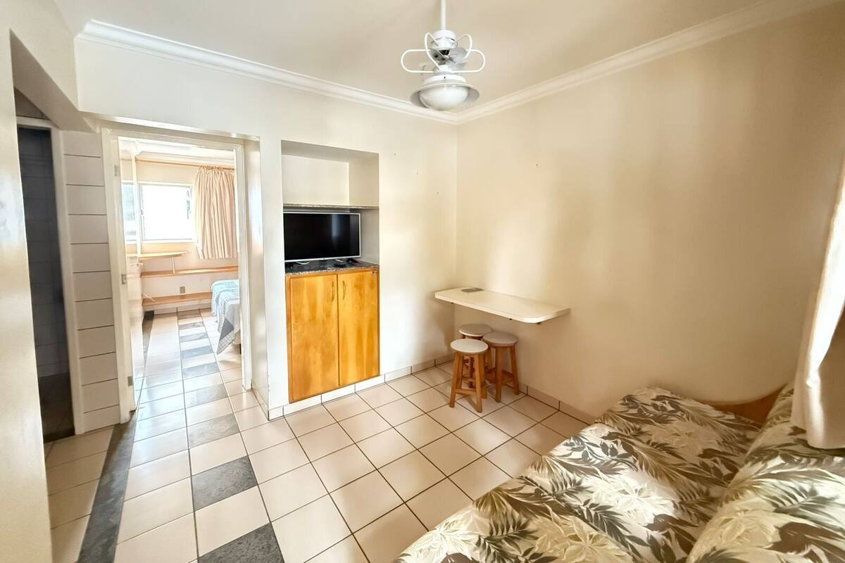 Quarto com cama, televisão, cozinha compacta e ventoinha no teto.