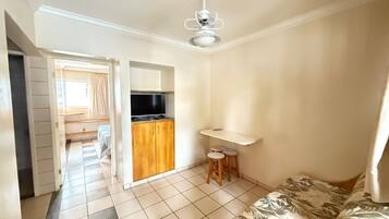 A room with a bed, a TV, a kitchenette, and a ceiling fan.