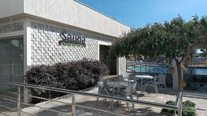 A building with a brick wall and a pool area with outdoor seating. - DiRoma International Resort Via Caldas (Caldas Novas)