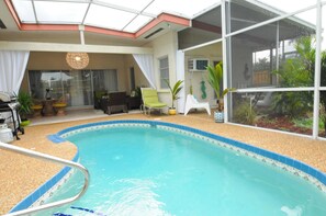 An indoor swimming pool with a glass ceiling, surrounded by lounge chairs and a dining area.