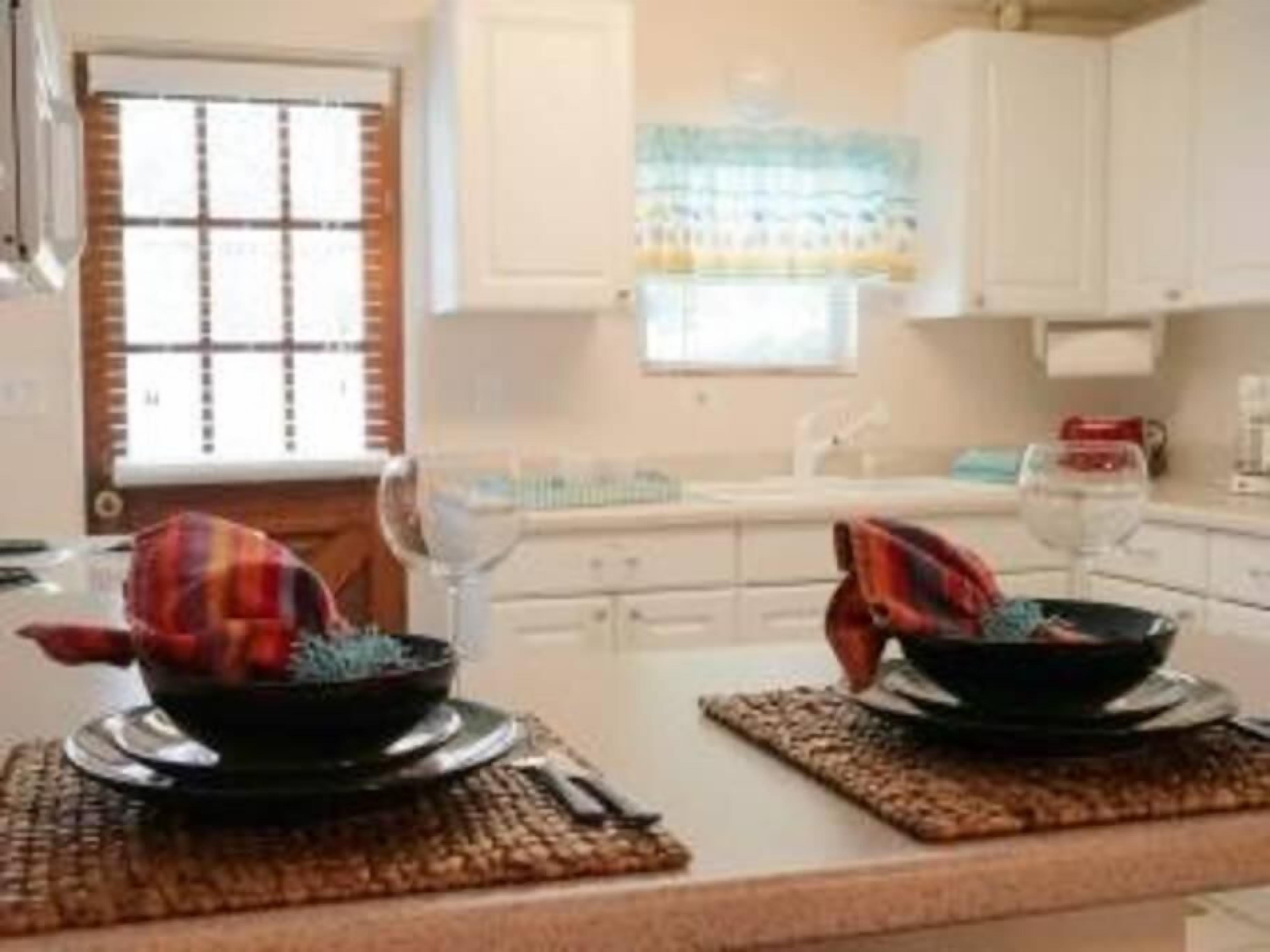 A kitchen with white cabinets, a window with blinds, and a countertop with two bowls and a wine glass.
