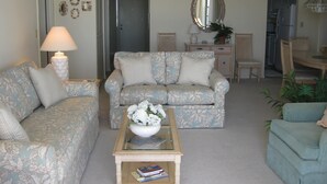 A living room with floral patterned sofas, a coffee table with a vase of flowers, and a dining area with chairs and a table. - South Seas Tower 3 606 (Marco Island)