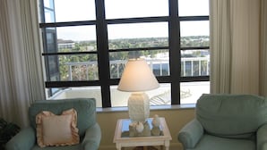 A room with two green armchairs, a small white table with a lamp, and a view through large windows. - South Seas Tower 3 606 (Marco Island)