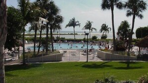 A pool area with palm trees, a view of the ocean, and a beach in the background. - South Seas Tower 3 606 (Marco Island)