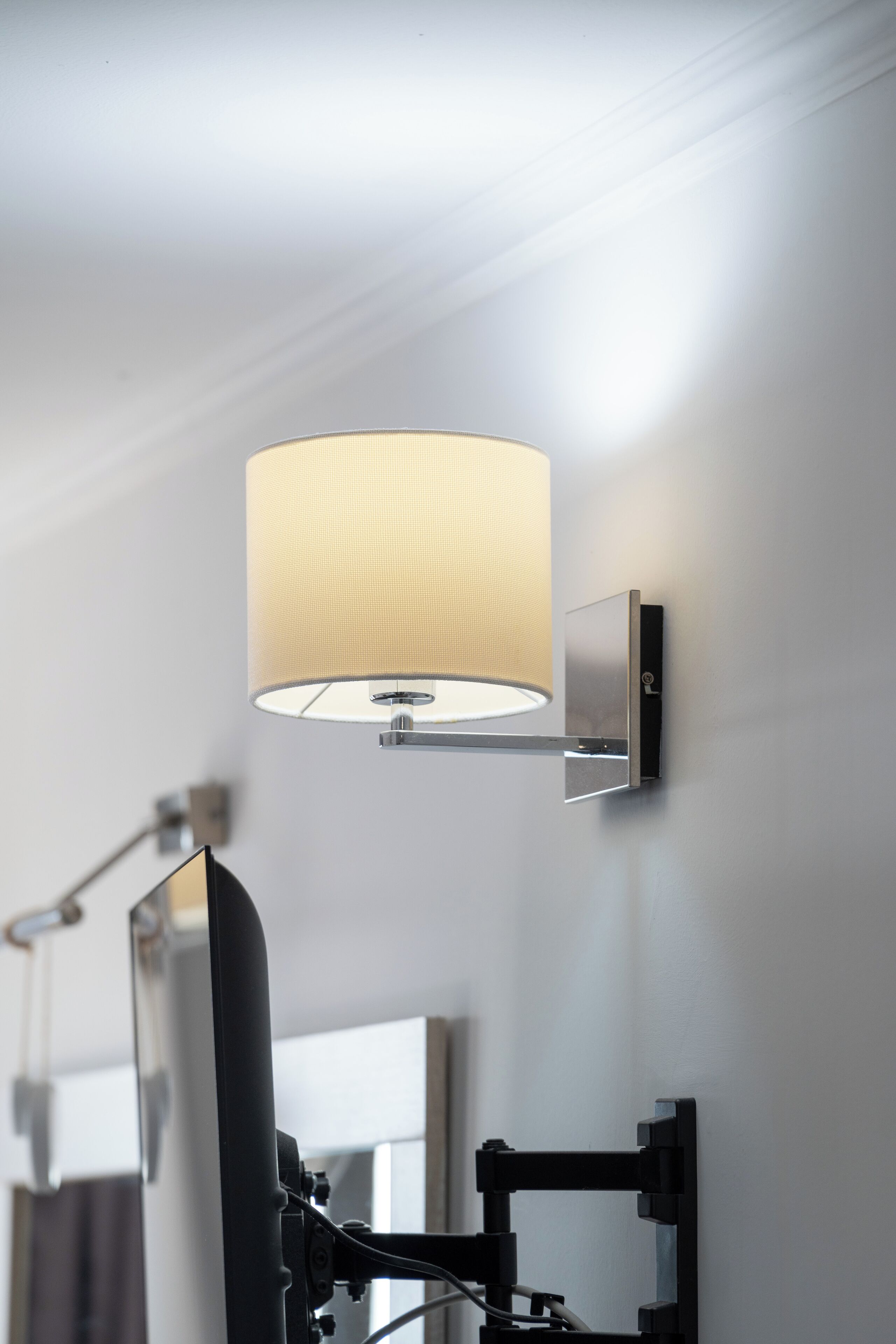 A modern wall-mounted lamp with a cylindrical shade, a flat-screen TV, and a mirror.