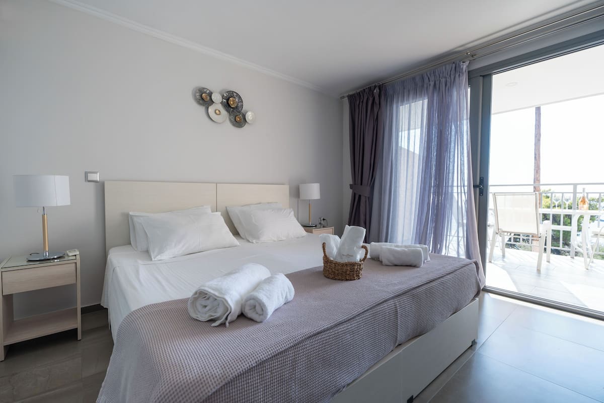 A hotel room with a large bed, two bedside tables, a wall clock, and a view of the outdoors.