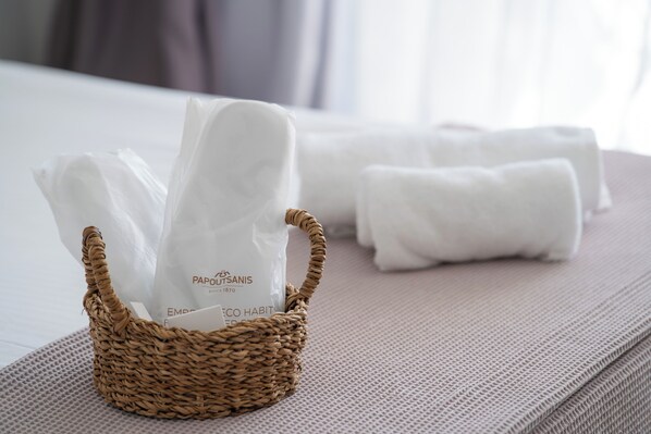 A wicker basket with a white plastic bag and rolled white towels on a textured surface. - La Luna Hotel (Skiathos)