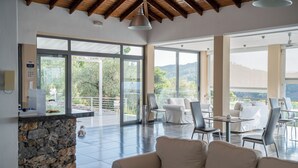 Amplia sala de estar con una pared de piedra decorativa, ventanas grandes y un balcón con vistas a un paisaje pintoresco.