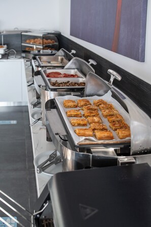 A buffet setup with various food items in trays, including pastries and a hot dish.