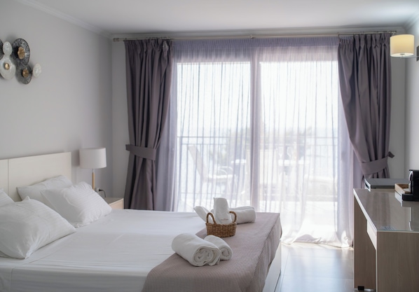 A hotel room with a neatly made bed, a bedside table with a lamp, and a window with curtains. - La Luna Hotel (Skiathos)
