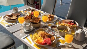 Una mesa de desayuno con diferentes platos, una cafetera y vista a la piscina y la playa.