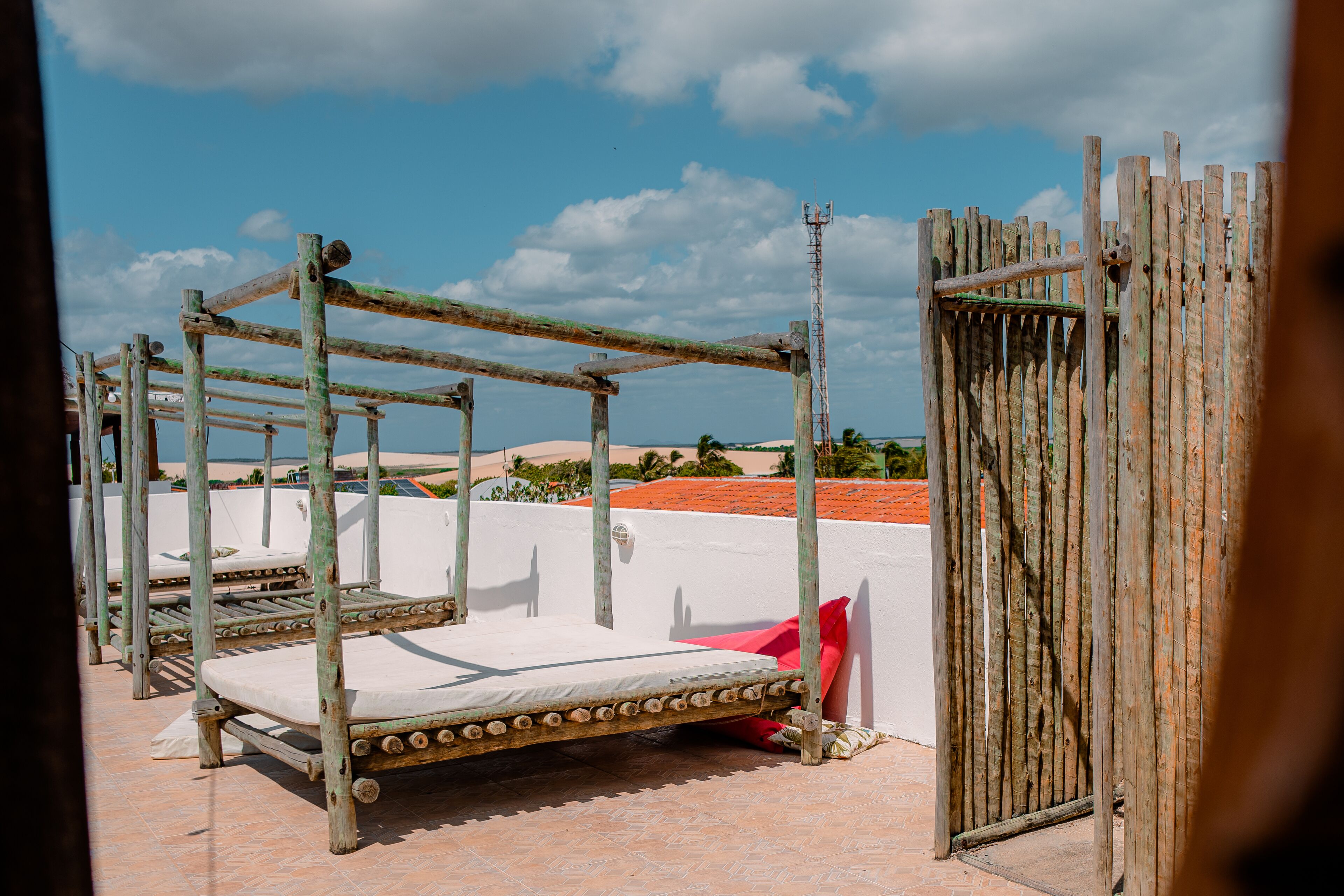 A rustic outdoor sleeping area with wooden beds and a high fence.
