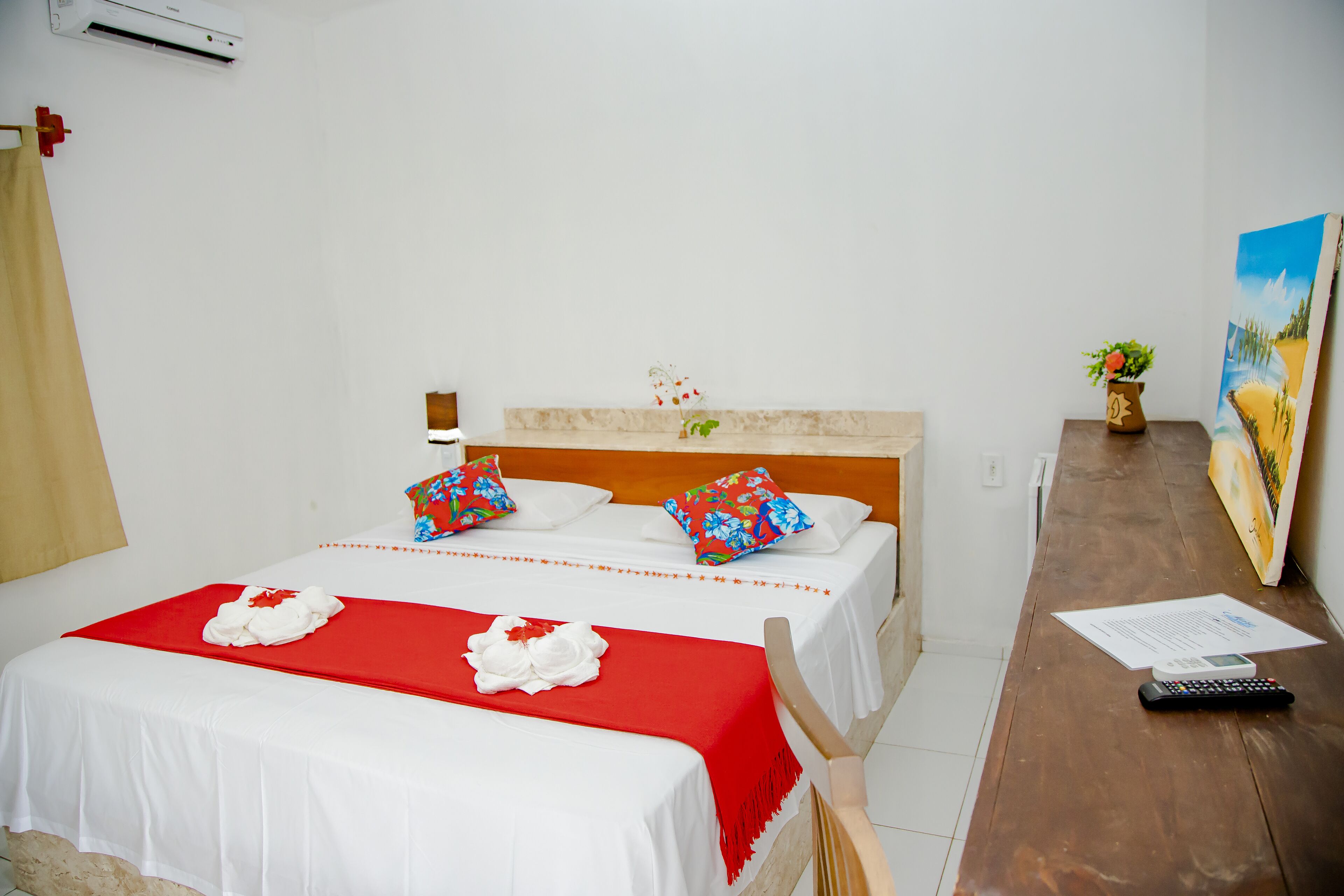 Una habitación de hotel con dos camas, un escritorio de madera, un cuadro y una planta pequeña.